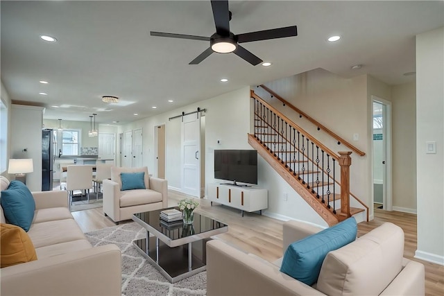 living room featuring light wood-type flooring, a barn door, and ceiling fan