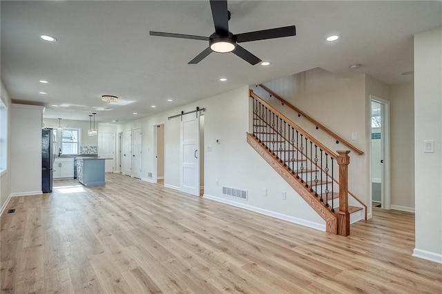 unfurnished living room with a barn door, ceiling fan, and light wood-type flooring