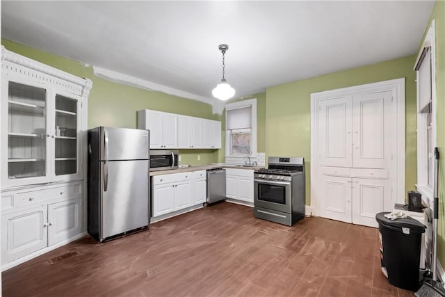 kitchen with white cabinetry, dark wood-type flooring, stainless steel appliances, and decorative light fixtures