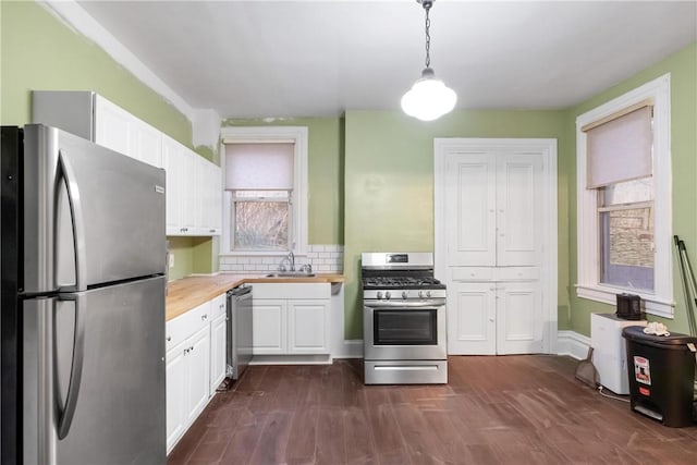 kitchen featuring stainless steel appliances, sink, white cabinets, butcher block countertops, and hanging light fixtures