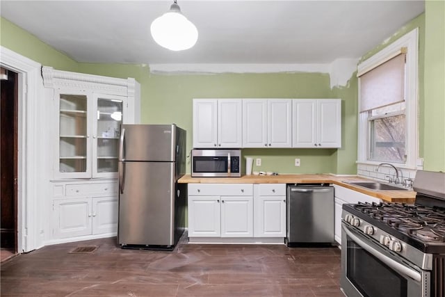 kitchen with stainless steel appliances, sink, pendant lighting, white cabinetry, and butcher block counters