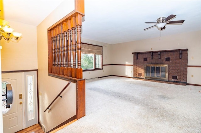 unfurnished living room featuring a fireplace, ceiling fan with notable chandelier, and light colored carpet