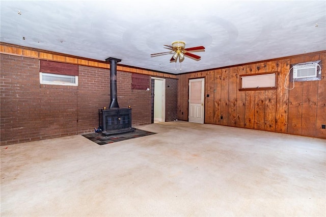 unfurnished living room with ornamental molding, brick wall, a wall unit AC, ceiling fan, and a wood stove