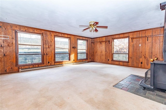 unfurnished living room featuring light carpet, a wood stove, ceiling fan, and a healthy amount of sunlight