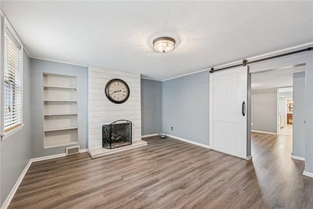 unfurnished living room featuring a large fireplace, hardwood / wood-style flooring, and a barn door