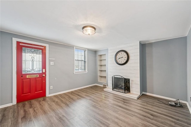 unfurnished living room with a large fireplace, crown molding, built in features, and hardwood / wood-style floors