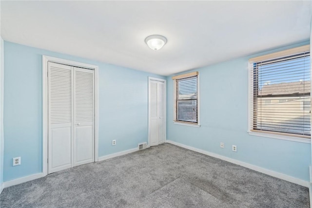 unfurnished bedroom with two closets, light colored carpet, and multiple windows