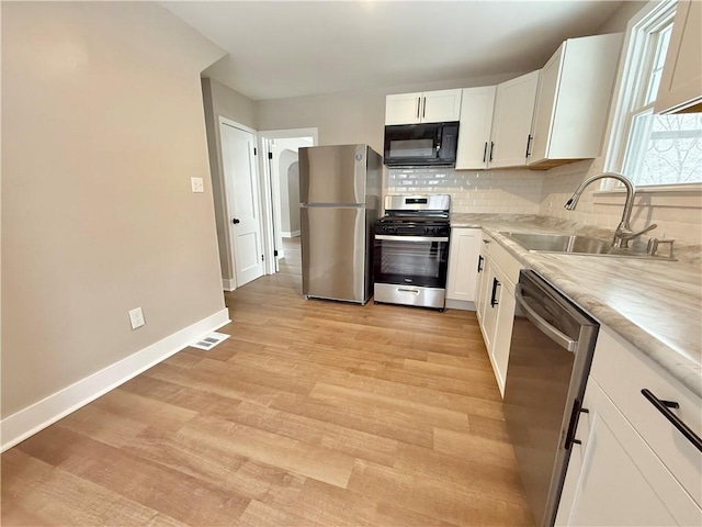 kitchen with sink, light hardwood / wood-style flooring, decorative backsplash, white cabinets, and appliances with stainless steel finishes