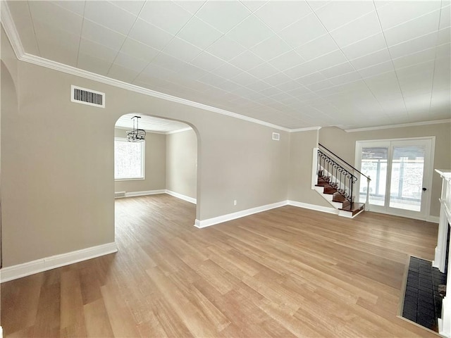 unfurnished living room featuring light hardwood / wood-style flooring, a brick fireplace, crown molding, and a notable chandelier