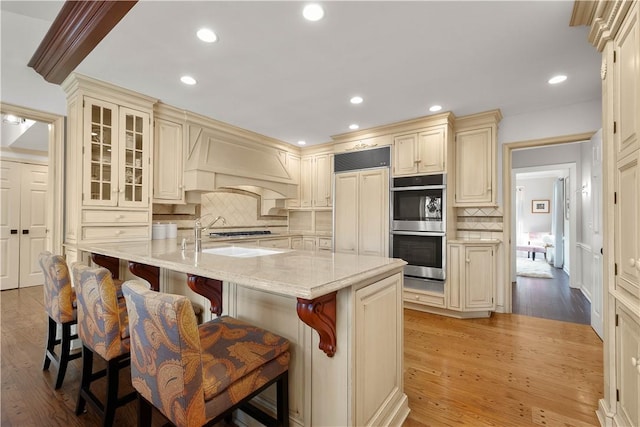 kitchen featuring a kitchen island with sink, cream cabinets, decorative backsplash, light stone counters, and a kitchen bar