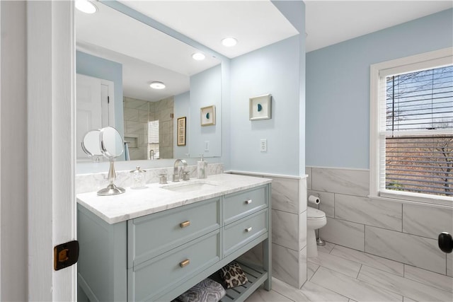 bathroom with vanity, toilet, a wealth of natural light, and tile walls