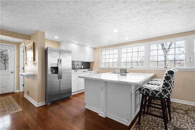 kitchen featuring white cabinets, decorative backsplash, stainless steel fridge with ice dispenser, and a textured ceiling