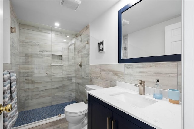 bathroom with tiled shower, vanity, tile walls, and toilet