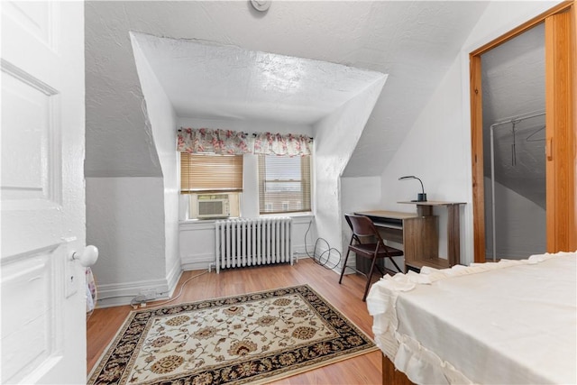 bedroom with a closet, radiator heating unit, a textured ceiling, and light hardwood / wood-style flooring