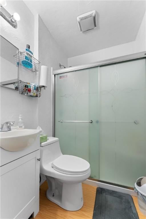 bathroom with a shower with door, vanity, wood-type flooring, and toilet