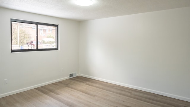 spare room with light wood-type flooring and a textured ceiling