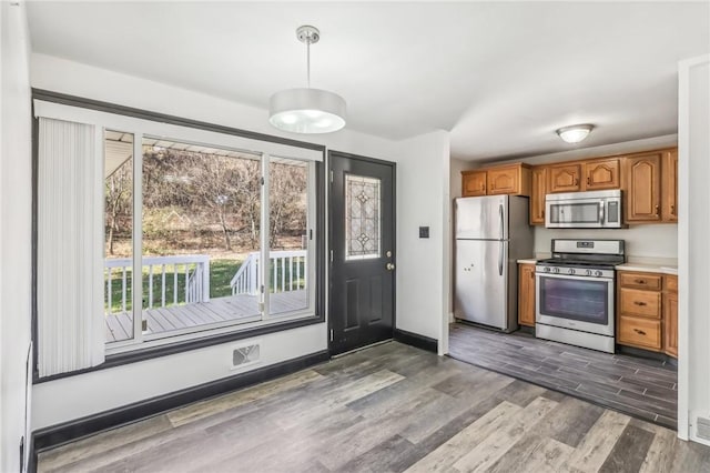 kitchen featuring appliances with stainless steel finishes, hanging light fixtures, and dark wood-type flooring