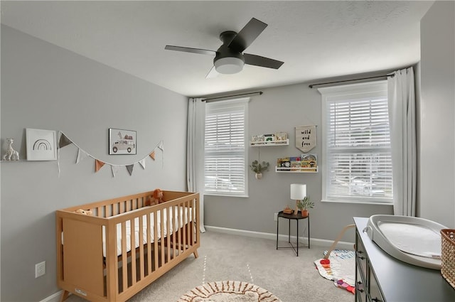 carpeted bedroom with ceiling fan, multiple windows, and a nursery area