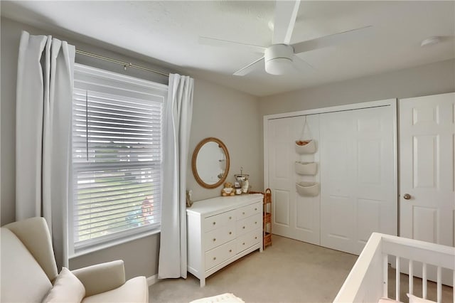 bedroom featuring ceiling fan, a crib, light carpet, and a closet