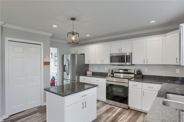 kitchen featuring stainless steel appliances, crown molding, wood-type flooring, decorative light fixtures, and white cabinets