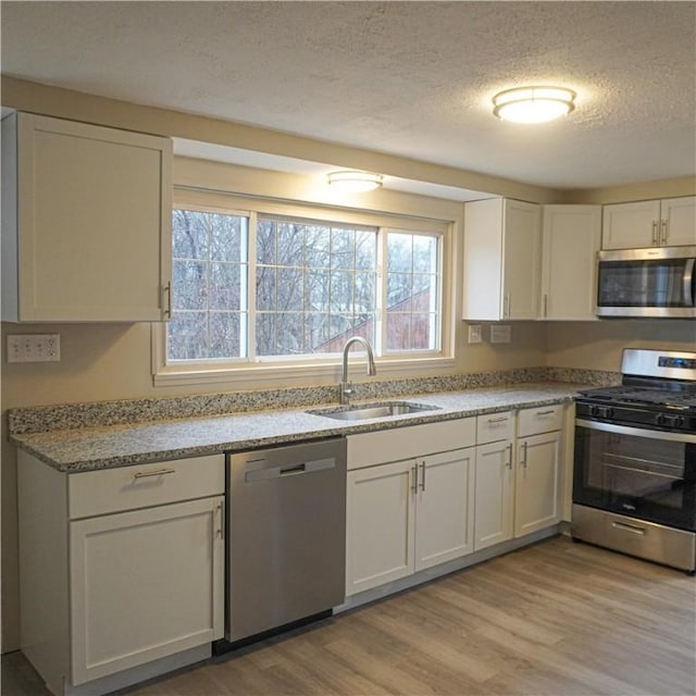 kitchen featuring light stone counters, stainless steel appliances, sink, light hardwood / wood-style flooring, and white cabinets