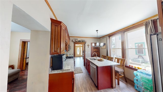 kitchen with hardwood / wood-style floors, ornamental molding, an island with sink, appliances with stainless steel finishes, and decorative light fixtures