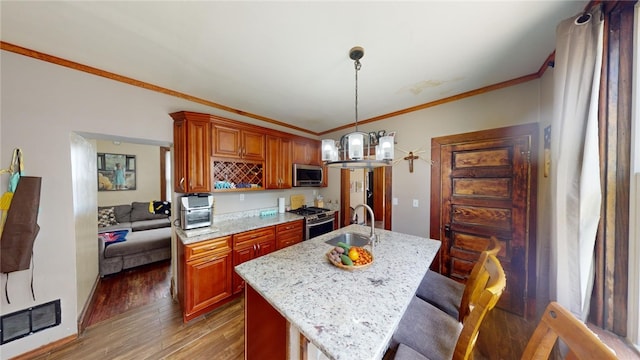 kitchen with appliances with stainless steel finishes, dark wood-type flooring, sink, pendant lighting, and an island with sink