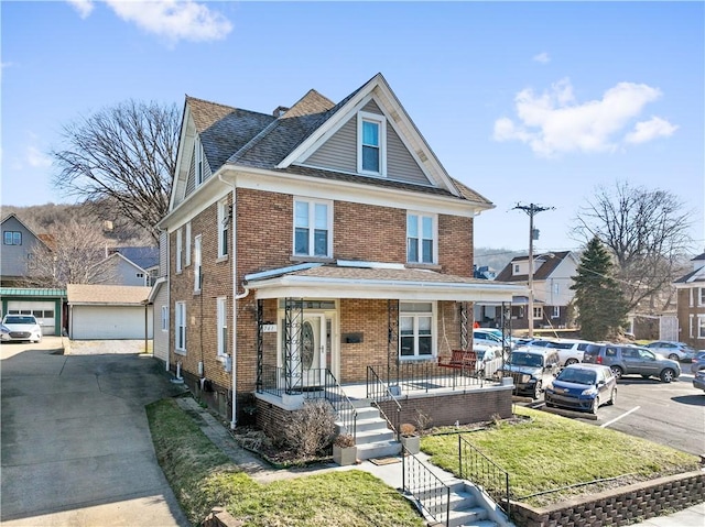 traditional style home featuring brick siding, a front yard, an outdoor structure, and roof with shingles