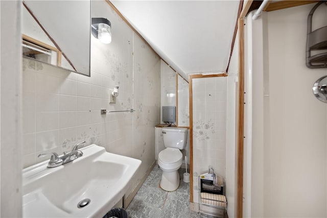 bathroom featuring toilet, a sink, and tile walls