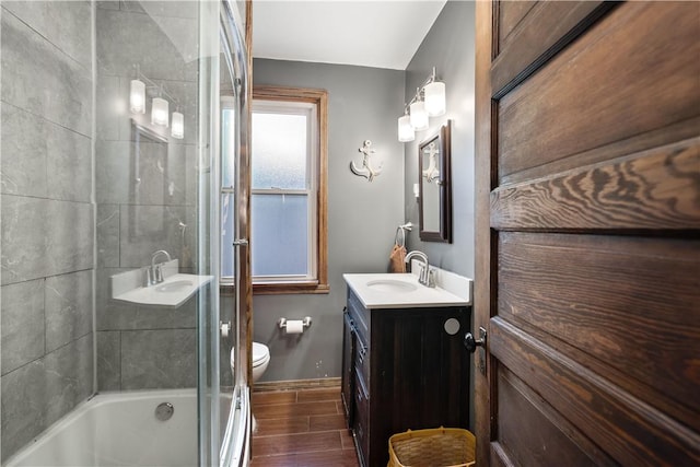 full bath featuring vanity, baseboards, enclosed tub / shower combo, toilet, and wood finished floors