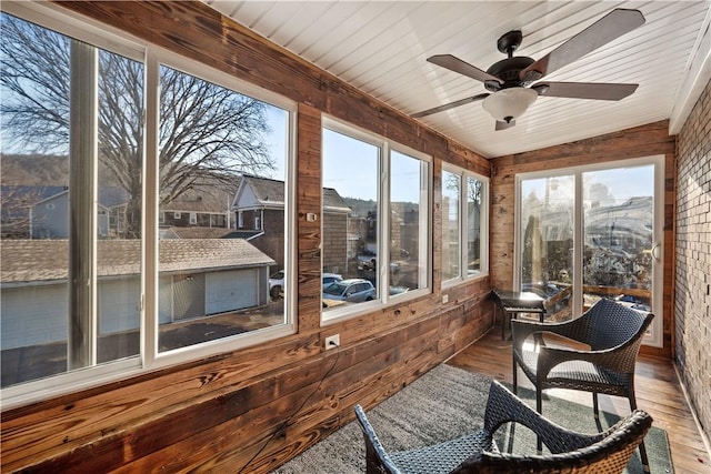 sunroom with wood walls, wood-type flooring, and a ceiling fan