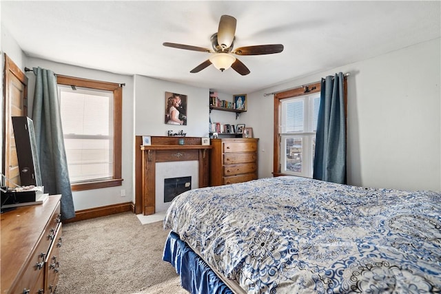 bedroom featuring light carpet, ceiling fan, baseboards, and a glass covered fireplace