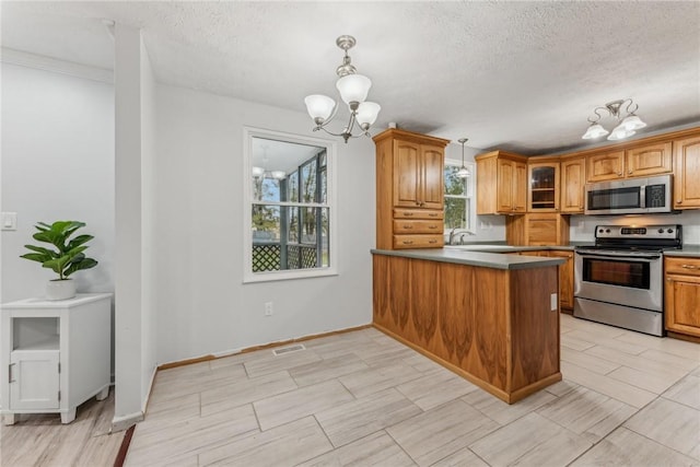 kitchen with an inviting chandelier, kitchen peninsula, a textured ceiling, decorative light fixtures, and appliances with stainless steel finishes