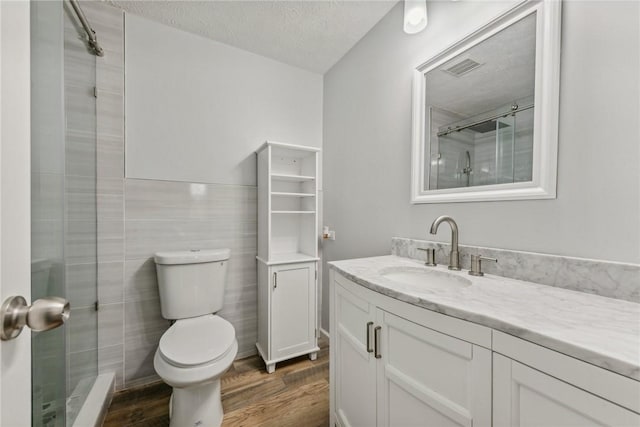 bathroom with a textured ceiling, vanity, a shower with shower door, tile walls, and hardwood / wood-style flooring