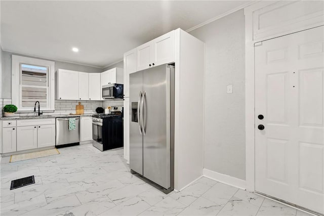 kitchen featuring backsplash, ornamental molding, stainless steel appliances, sink, and white cabinetry