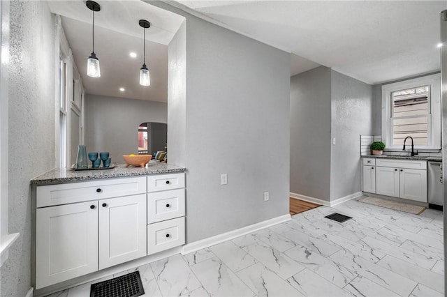 kitchen featuring light stone countertops, stainless steel dishwasher, sink, pendant lighting, and white cabinets