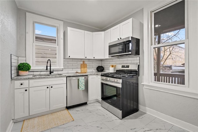 kitchen with light stone counters, ornamental molding, stainless steel appliances, sink, and white cabinetry