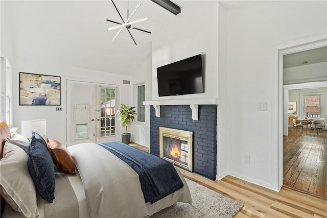 bedroom with access to exterior, an inviting chandelier, vaulted ceiling with beams, light hardwood / wood-style flooring, and a fireplace