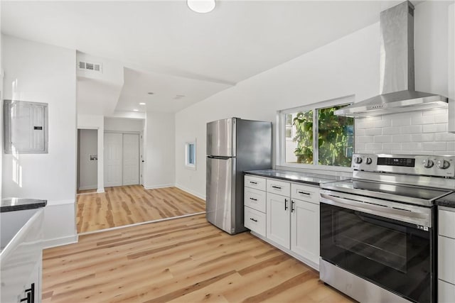 kitchen with wall chimney exhaust hood, electric panel, appliances with stainless steel finishes, white cabinets, and light wood-type flooring