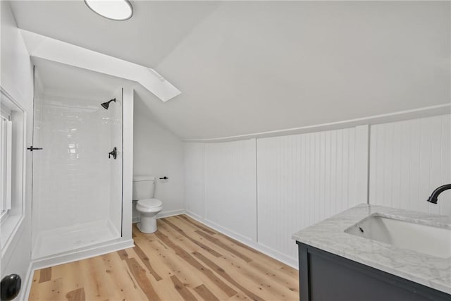 bathroom featuring vanity, lofted ceiling with skylight, tiled shower, hardwood / wood-style flooring, and toilet