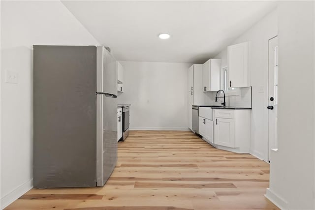 kitchen with white cabinetry, sink, backsplash, appliances with stainless steel finishes, and light wood-type flooring