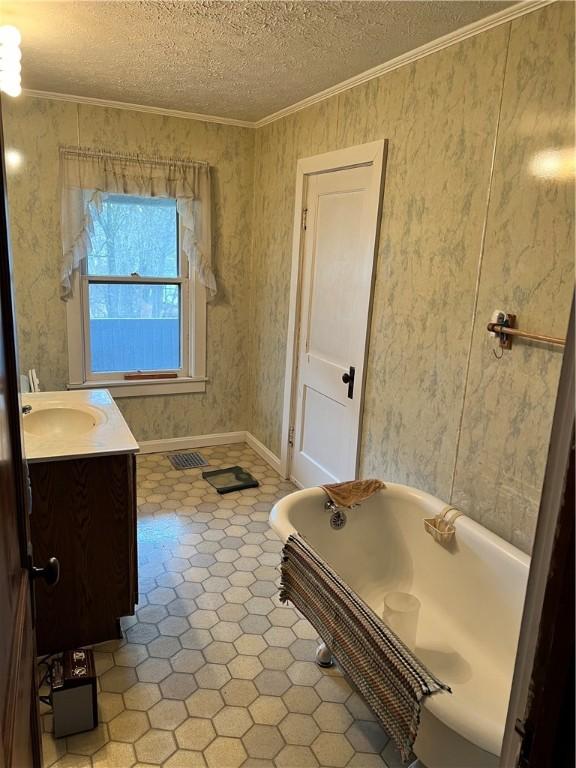 bathroom featuring a textured ceiling, vanity, crown molding, and a tub