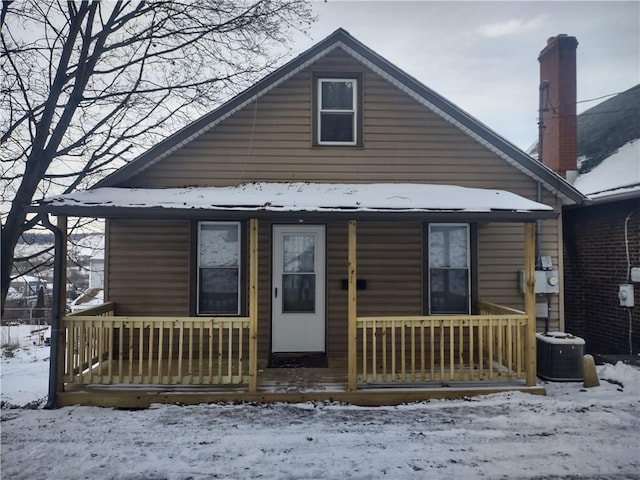 snow covered rear of property with covered porch and central air condition unit