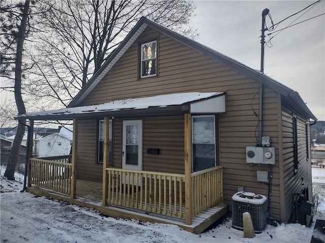 snow covered house with cooling unit and covered porch