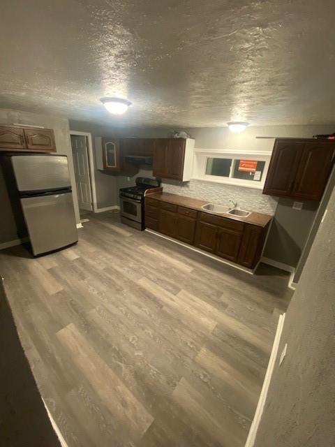 kitchen with sink, a textured ceiling, light wood-type flooring, appliances with stainless steel finishes, and backsplash