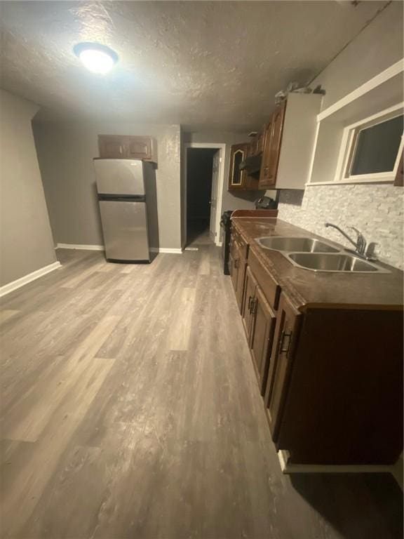 kitchen with stainless steel refrigerator, sink, backsplash, a textured ceiling, and light hardwood / wood-style flooring