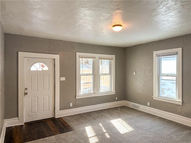 foyer entrance with dark carpet and a textured ceiling