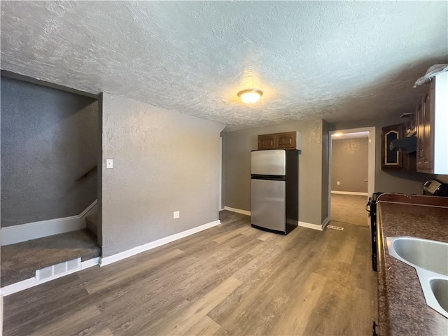 kitchen featuring stainless steel refrigerator, sink, hardwood / wood-style floors, and a textured ceiling