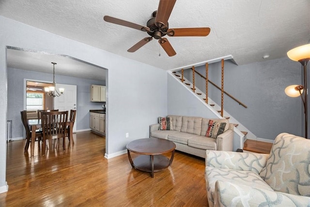 living room with ceiling fan with notable chandelier, wood-type flooring, and a textured ceiling