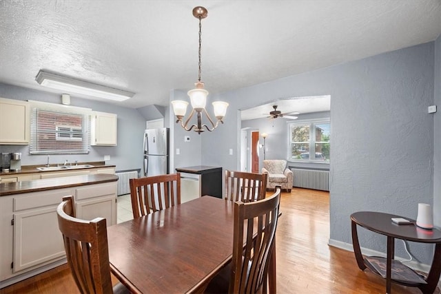 dining room featuring ceiling fan with notable chandelier, sink, radiator, and light hardwood / wood-style flooring